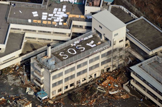 Люди, ждущие помощи на крыше здания, выложив надпись "SOS"  Кесеннума, Префектура Мияги, 12 марта 2011 (Фото - Yomiuri/Reuters)